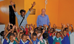 Bob Nameng raises his hands in joy with the children of the Soweto Kliptown Youth Centre while Zest WEG Group MD Louis Meiring looks on.
